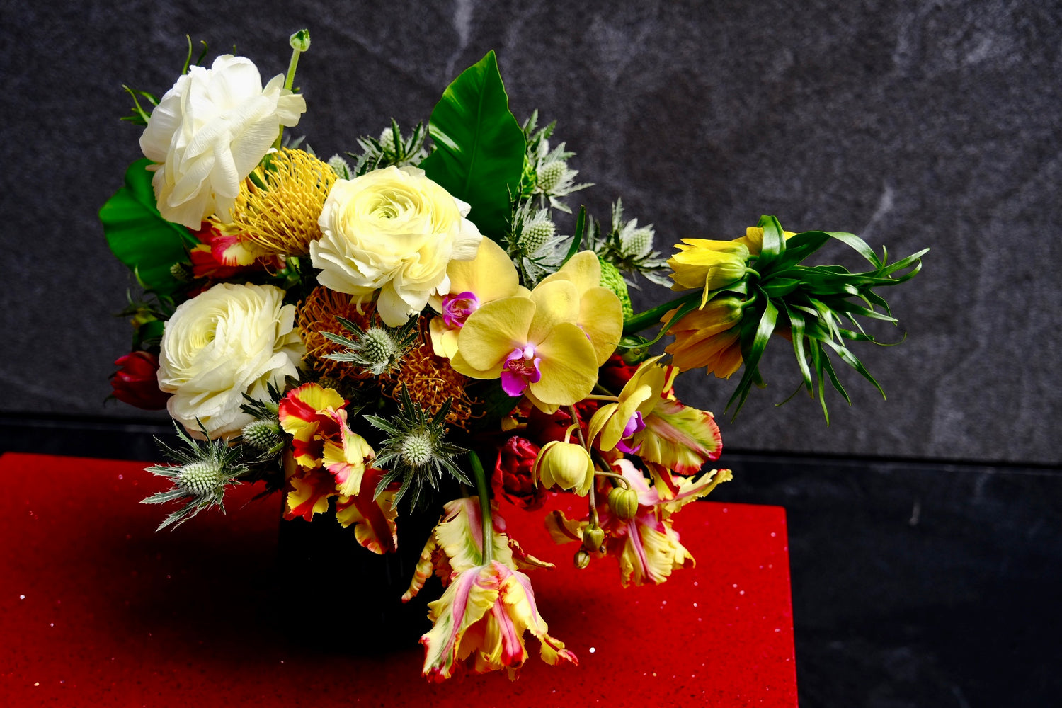 To honor the archetypal fervor of this Spanish American immigrant, we make this arrangement using red and yellows colors through different orchids, tulips, pincushions, thistle, ranunculus
