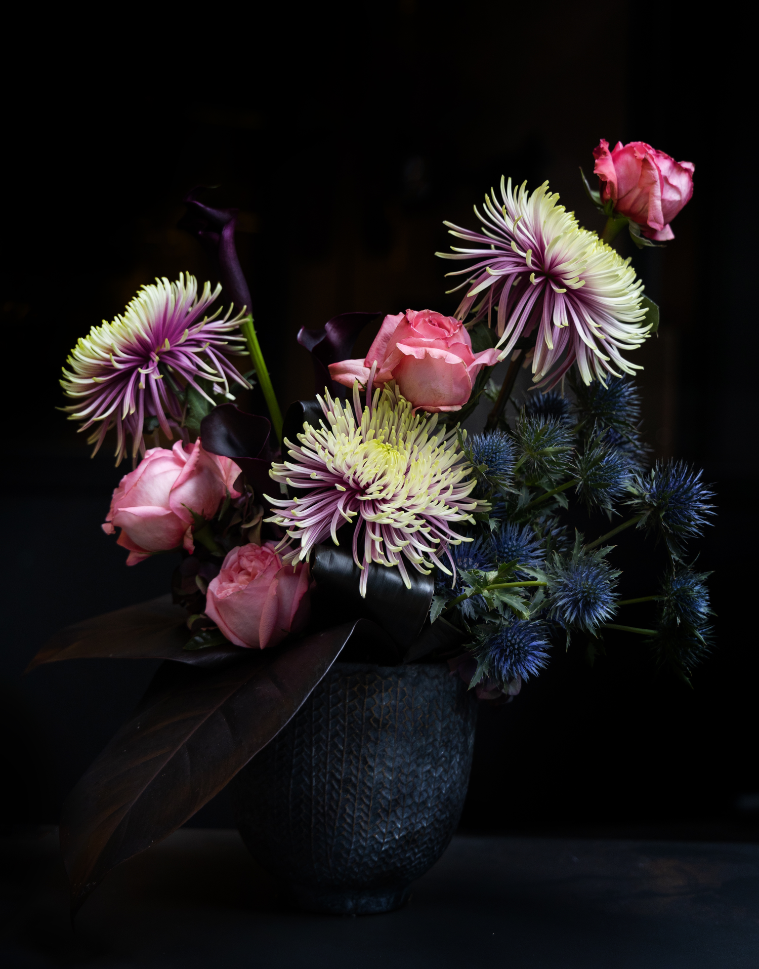 this sober and elegant arrangement brings together a group of submerged Sea holly eryngoes, protecting its beautiful purple under the shade of daring flowering chrysanthemums, and four burning roses.