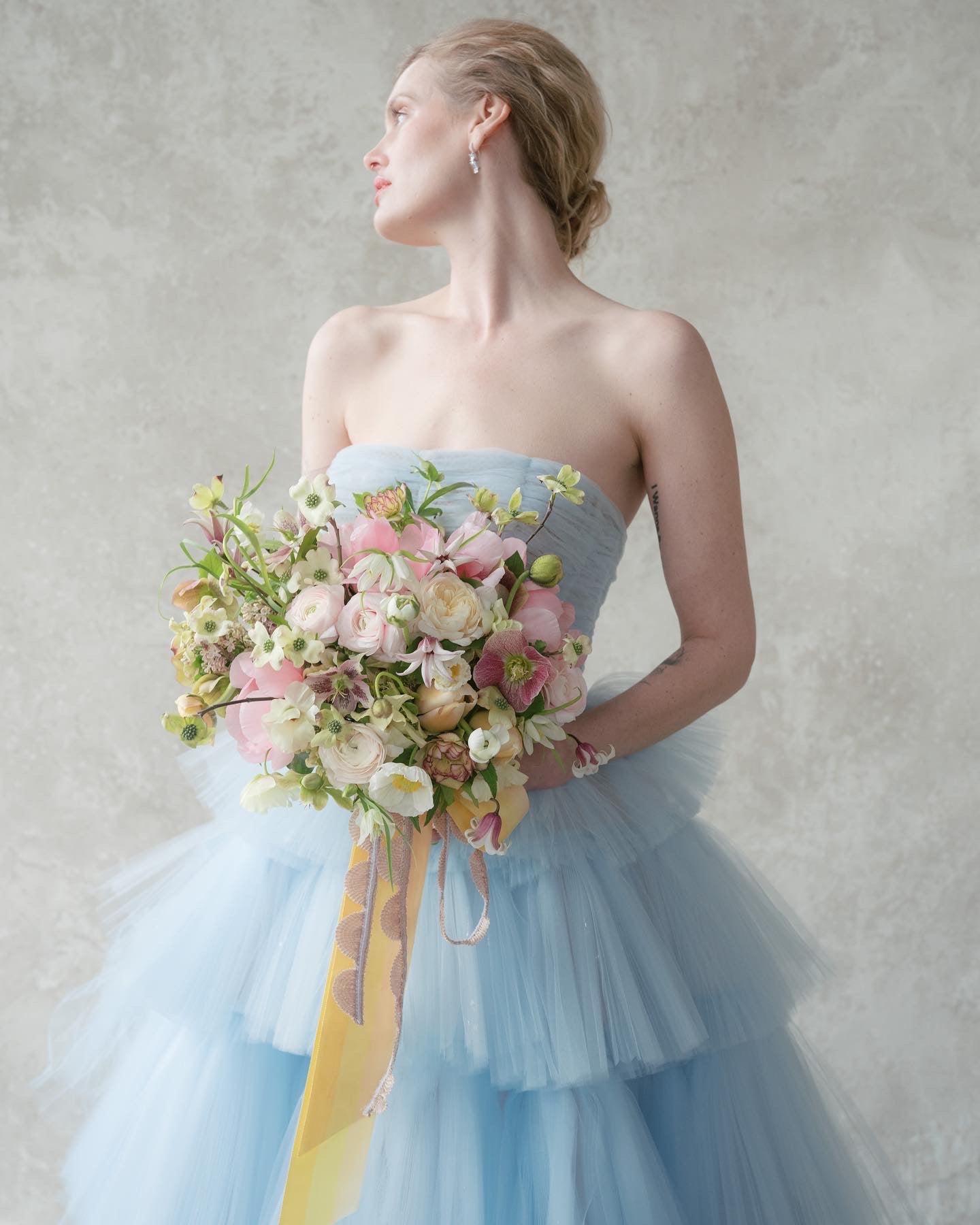 bride in a baby blue Oscar de la Renta dress holding a fresh flower bouquet.